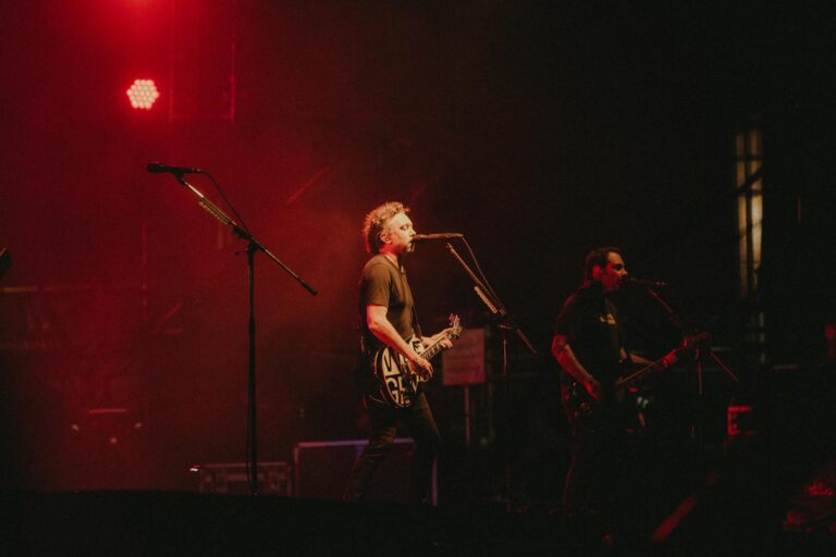 Live rock band performing on stage with vibrant red lighting creating a dynamic atmosphere.