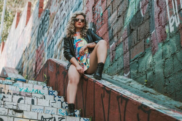 Stylish woman in biker jacket poses on colorful graffiti steps with urban flair.