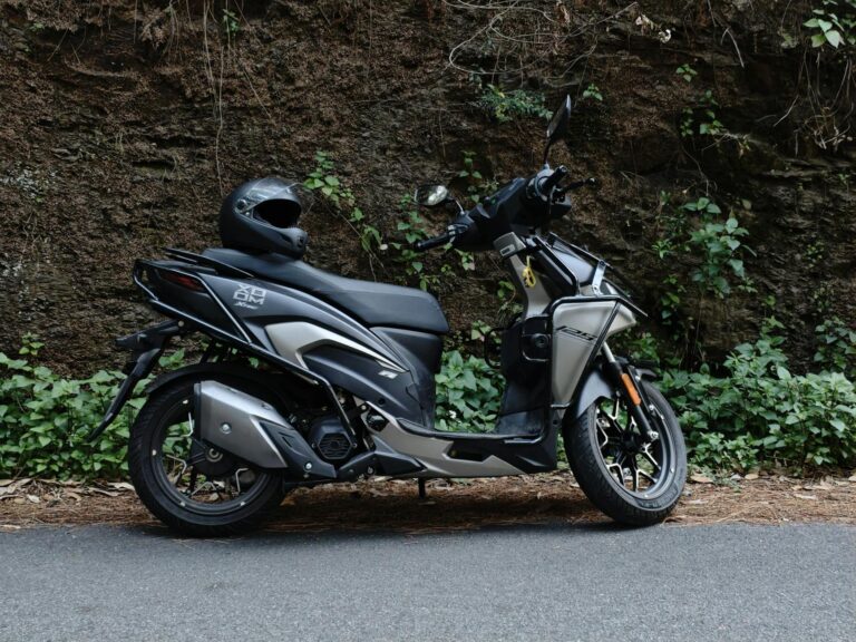 Black motor scooter with helmet parked beside a rock wall outdoors.