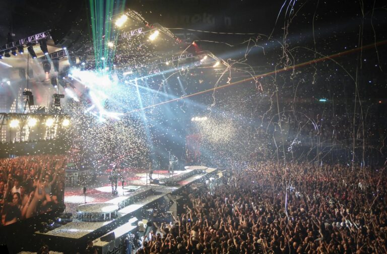 Vibrant concert scene with dynamic lighting, confetti, and a large enthusiastic crowd.