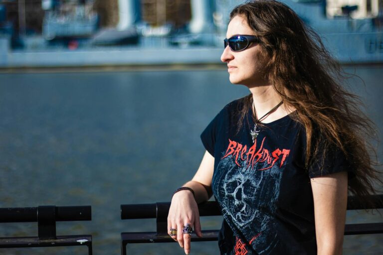 Woman wearing sunglasses and band T-shirt by the waterfront on a sunny day.