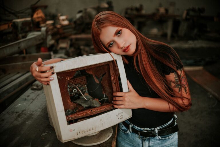A young woman leans on a broken vintage monitor in an industrial setting.
