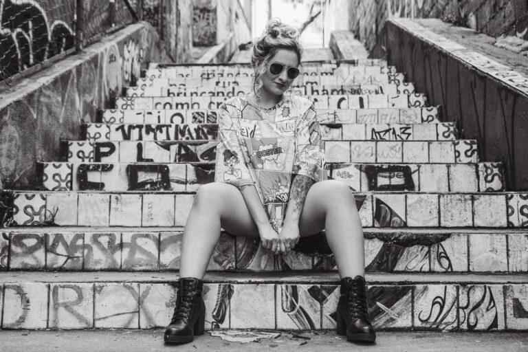 Black and white photo of a woman posing on graffiti-covered stairs wearing sunglasses.