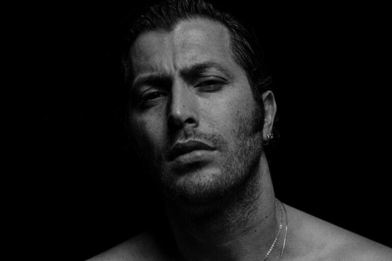 Intense black and white portrait of a bearded man with an earring, exuding moodiness.