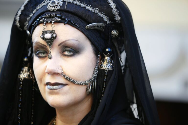 Close-up portrait of a woman in gothic attire with intricate headdress and jewelry.