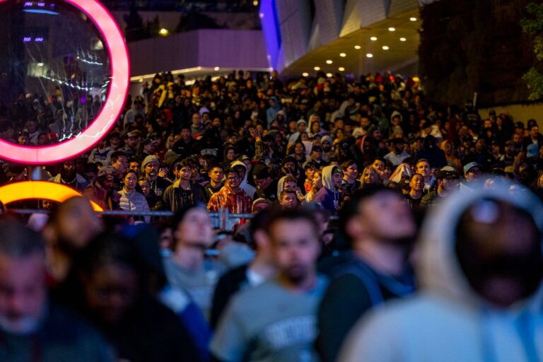 A lively crowd gathered outdoors at night under colorful lights.
