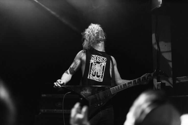 A powerful black and white image of a guitarist performing energetically on stage, creating an electrifying concert atmosphere.