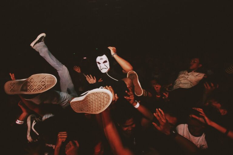 Vibrant scene of crowd surfing at a lively night concert with partygoers and a masked participant.