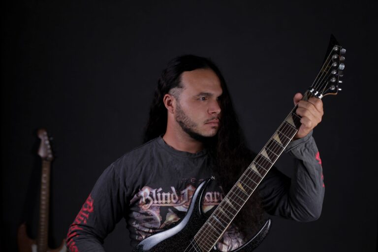 Musician with long hair playing electric guitar on stage in dark setting.