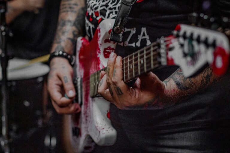 Tattooed hands skillfully play a red electric guitar during a live performance.