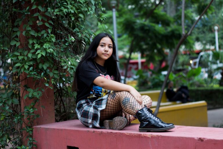 A young woman in punk fashion sits outdoors, showcasing a mix of style and attitude.