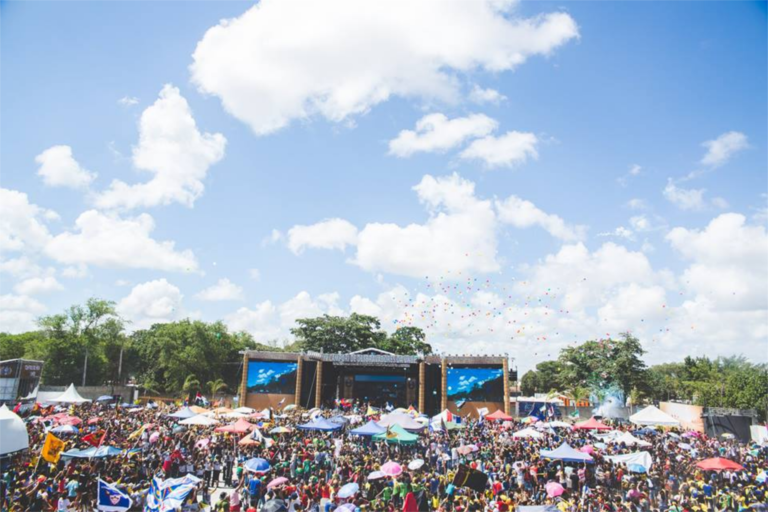 Lively outdoor festival with large crowd, vibrant umbrellas, and a clear sky in Santos Reis, Brazil.