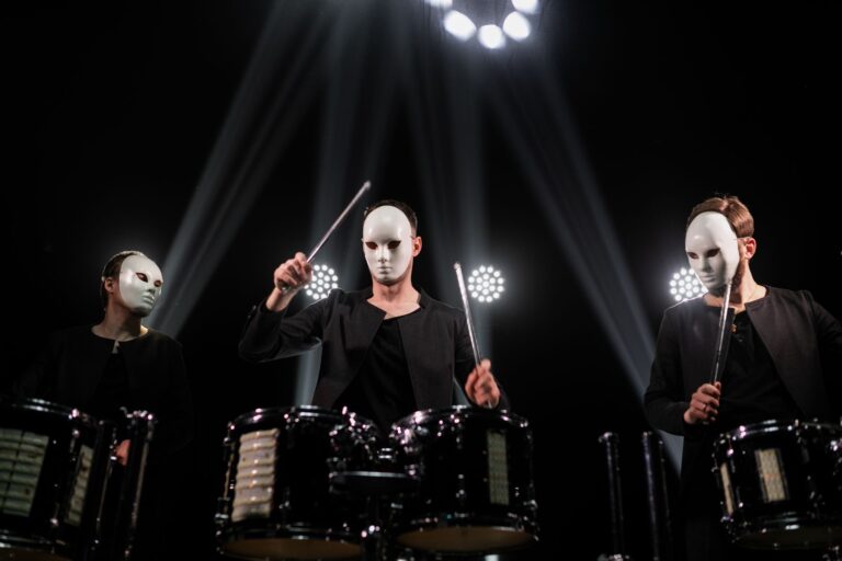 Three masked drummers in a powerful stage performance with dramatic lighting.