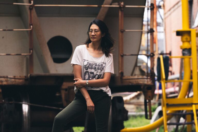 Stylish woman posing casually by industrial equipment outdoors.