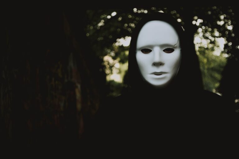 A mysterious figure in a white mask lurking in an ominous, dimly lit forest.
